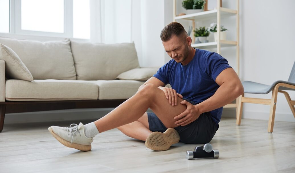 Man athlete pain and injury back arm and leg at home, sports injury bodybuilder, concept health and beauty